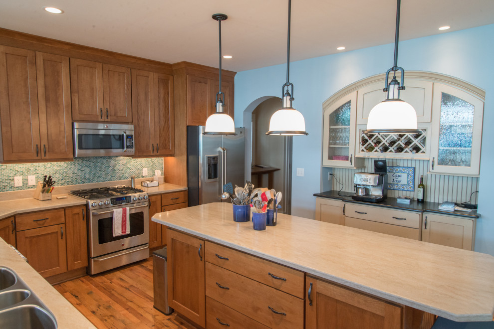Inspiration for a large beach style l-shaped eat-in kitchen in Chicago with a triple-bowl sink, shaker cabinets, medium wood cabinets, quartzite benchtops, blue splashback, glass tile splashback, stainless steel appliances, medium hardwood floors, with island, brown floor and beige benchtop.