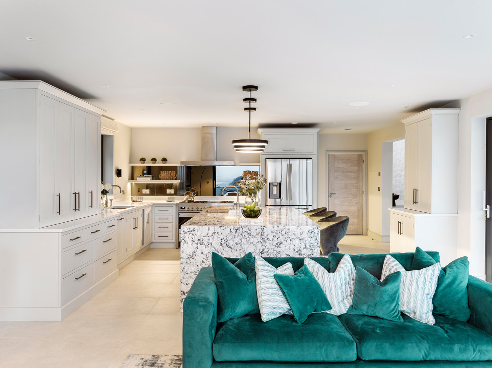 Expansive contemporary l-shaped open plan kitchen in Cornwall with a belfast sink, recessed-panel cabinets, green cabinets, quartz worktops, mirror splashback, integrated appliances, porcelain flooring, an island, white floors and multicoloured worktops.