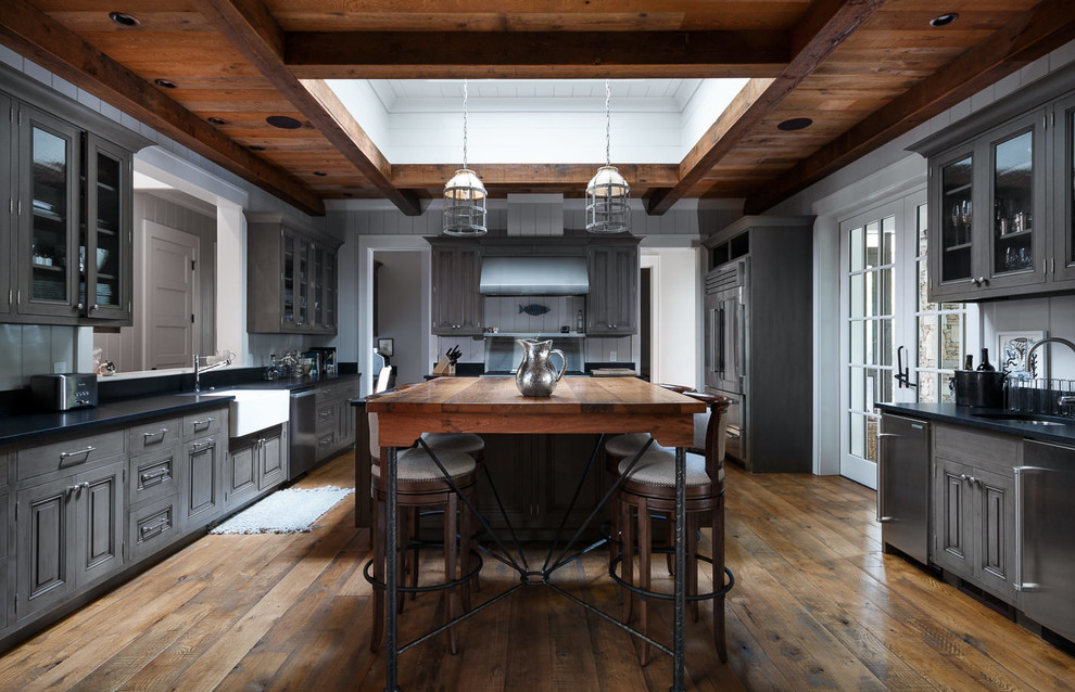 Mountain style dark wood floor and brown floor kitchen photo with a farmhouse sink, glass-front cabinets, gray cabinets and stainless steel appliances