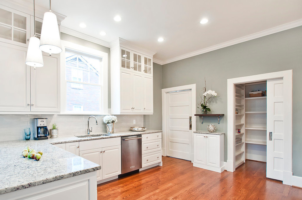 Photo of a large traditional u-shaped separate kitchen in Nashville with an undermount sink, raised-panel cabinets, white cabinets, granite benchtops, white splashback, ceramic splashback, stainless steel appliances, medium hardwood floors, a peninsula, brown floor and multi-coloured benchtop.