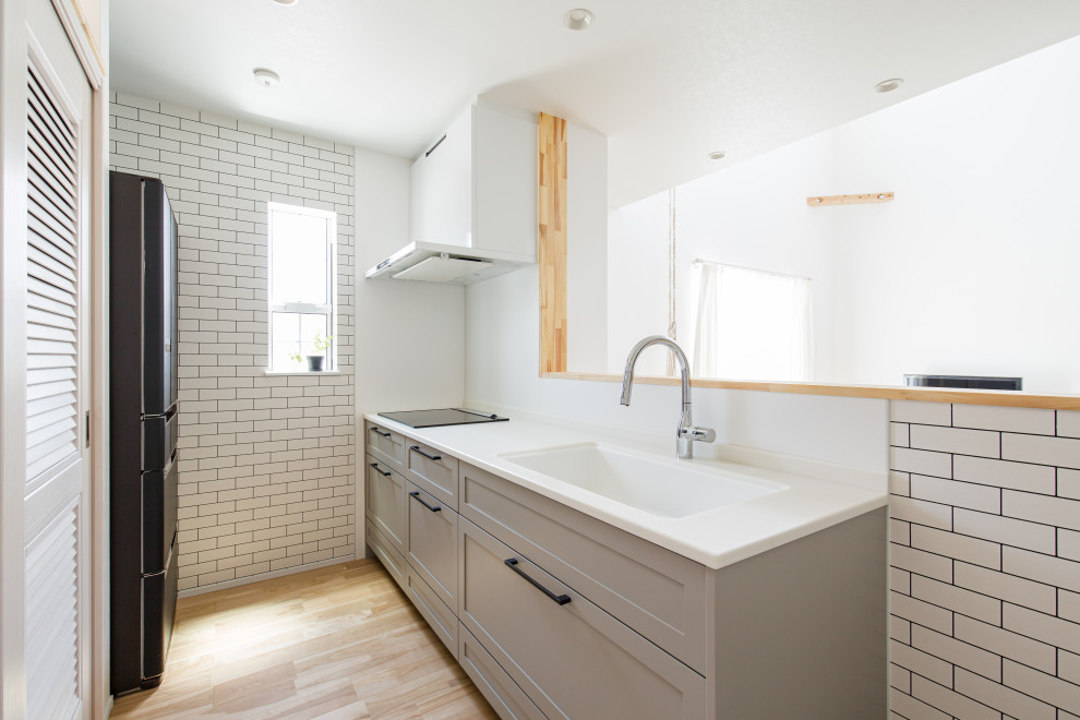 Maritim inredning av ett grå linjärt grått kök med öppen planlösning, med vita skåp, en köksö, en undermonterad diskho, luckor med lamellpanel, vitt stänkskydd, svarta vitvaror, mellanmörkt trägolv och brunt golv