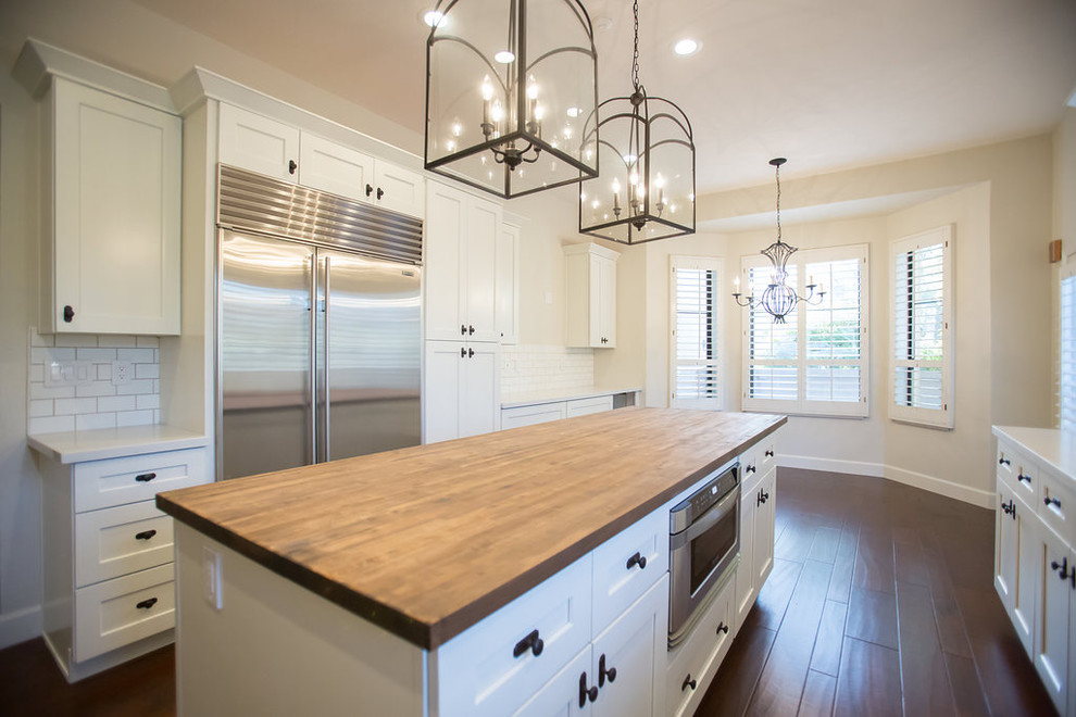 Example of a mid-sized transitional u-shaped dark wood floor enclosed kitchen design in Phoenix with an undermount sink, shaker cabinets, white cabinets, quartz countertops, multicolored backsplash, porcelain backsplash, stainless steel appliances and an island