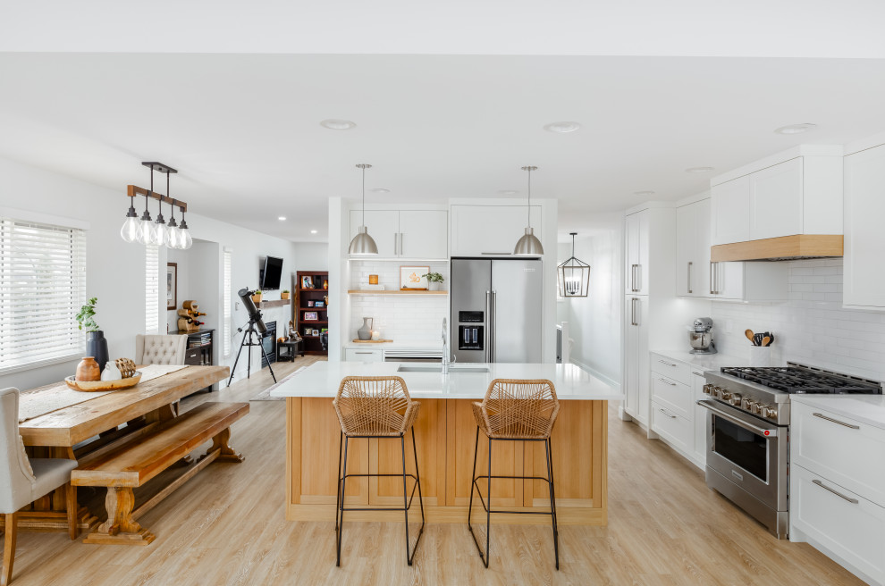 Eat-in kitchen - mid-sized transitional l-shaped light wood floor and beige floor eat-in kitchen idea in Vancouver with an undermount sink, shaker cabinets, white cabinets, quartzite countertops, white backsplash, subway tile backsplash, stainless steel appliances, an island and white countertops