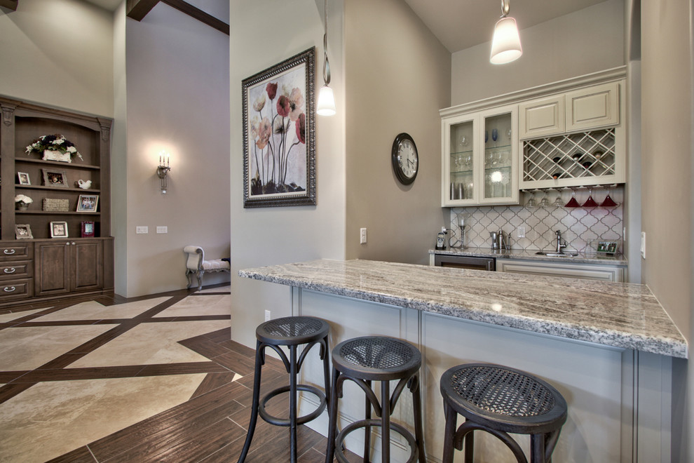 Inspiration for a mid-sized traditional single-wall seated home bar in Phoenix with an undermount sink, raised-panel cabinets, beige cabinets, granite benchtops, white splashback, ceramic splashback, dark hardwood floors, brown floor and grey benchtop.
