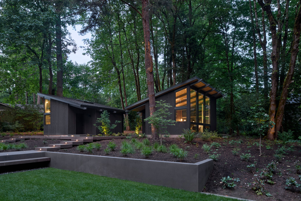 Inspiration for a large 1960s black one-story wood house exterior remodel in Portland with a shed roof, a shingle roof and a black roof