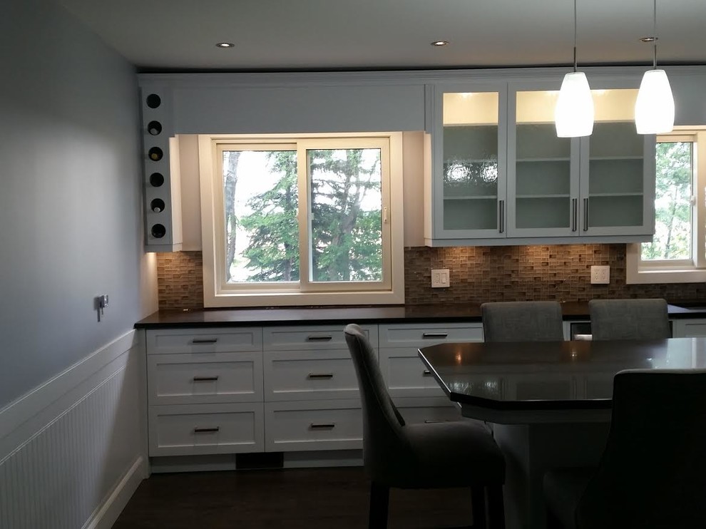 Example of a mid-sized transitional kitchen design with an undermount sink, shaker cabinets, white cabinets, brown backsplash, glass tile backsplash, stainless steel appliances and an island