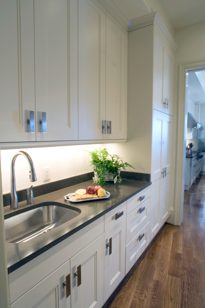 Example of a large transitional l-shaped light wood floor kitchen pantry design with an undermount sink, recessed-panel cabinets, white cabinets, quartz countertops, white backsplash, stone tile backsplash, stainless steel appliances and an island