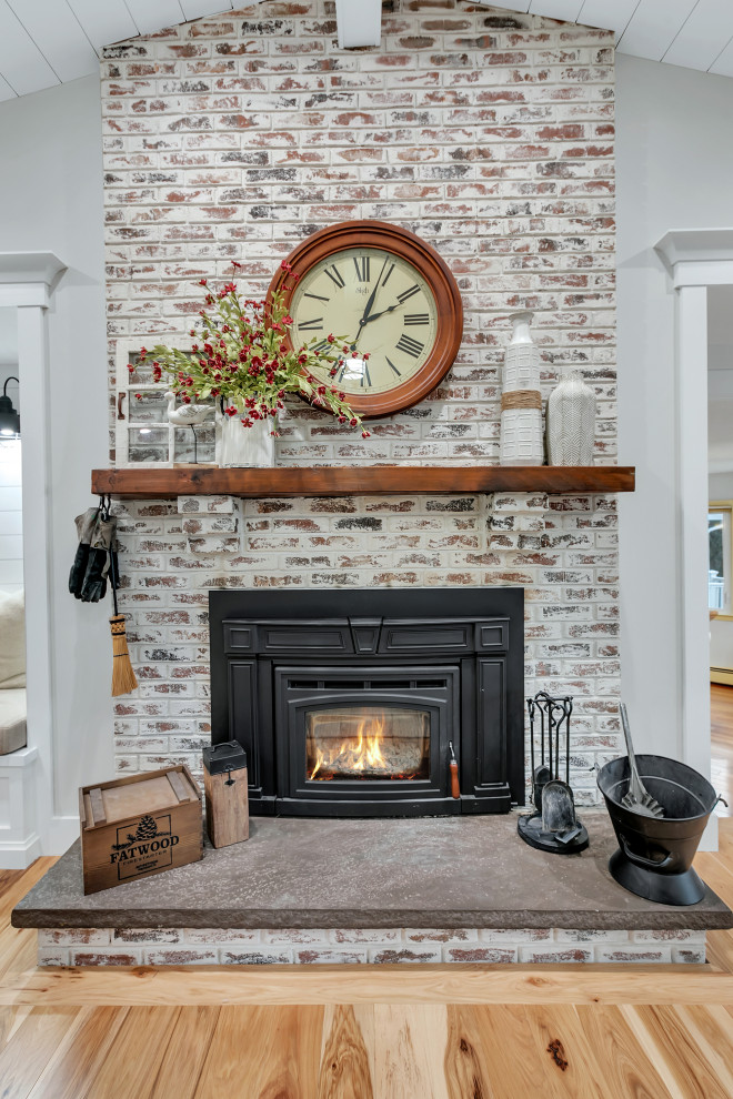 Inspiration for a mid-sized country enclosed living room in New York with a library, beige walls, light hardwood floors, a wood stove, a brick fireplace surround, a built-in media wall, brown floor and timber.