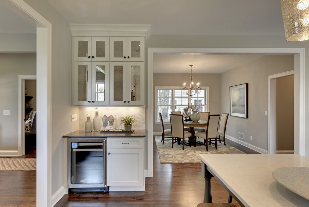 Inspiration for a large transitional u-shaped medium tone wood floor and brown floor eat-in kitchen remodel in Minneapolis with a farmhouse sink, flat-panel cabinets, white cabinets, quartz countertops, white backsplash, marble backsplash, stainless steel appliances and an island
