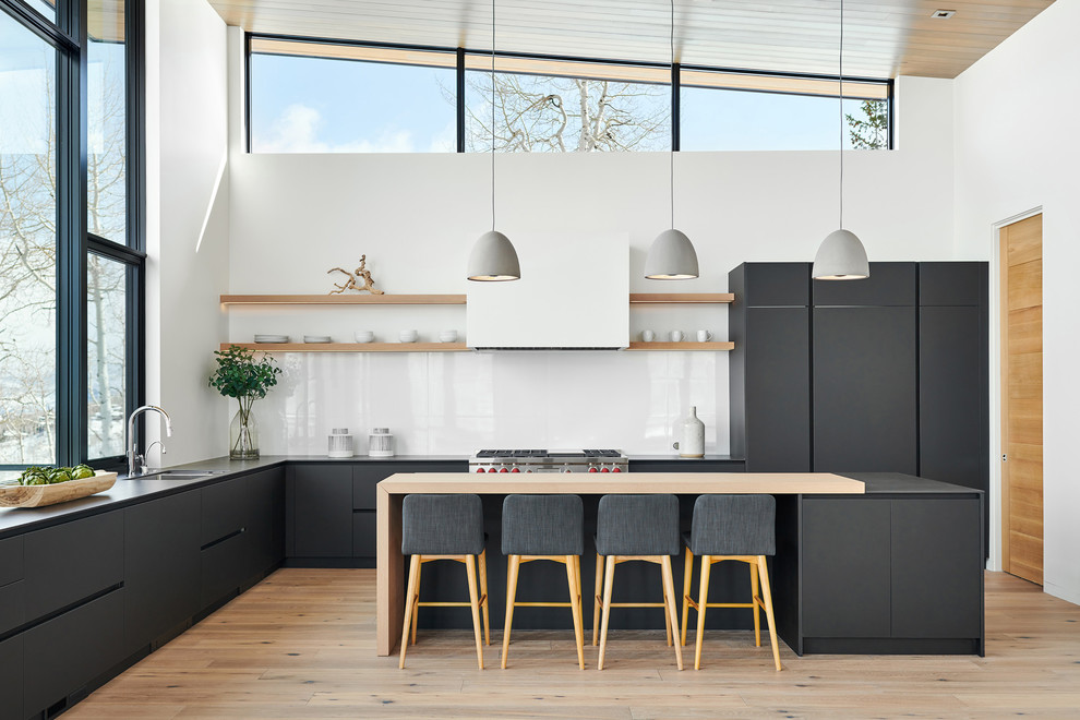 Design ideas for a large contemporary u-shaped eat-in kitchen in Denver with a double-bowl sink, flat-panel cabinets, black cabinets, white splashback, light hardwood floors, with island, beige floor, soapstone benchtops, stone slab splashback, panelled appliances and black benchtop.
