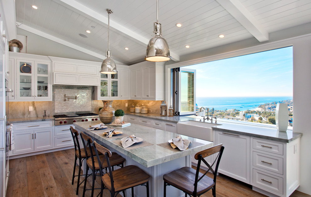 Large beach style u-shaped kitchen in Orange County with a farmhouse sink, recessed-panel cabinets, white cabinets, stone tile splashback, with island and medium hardwood floors.