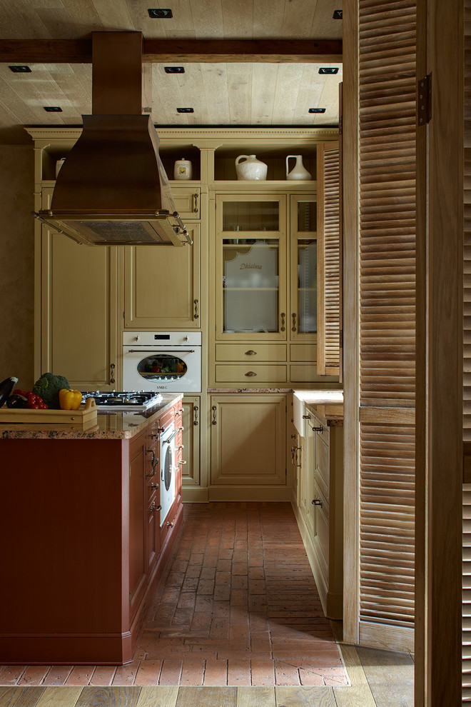 This is an example of a mediterranean l-shaped open plan kitchen in Moscow with a farmhouse sink, brick floors, with island, raised-panel cabinets and yellow cabinets.