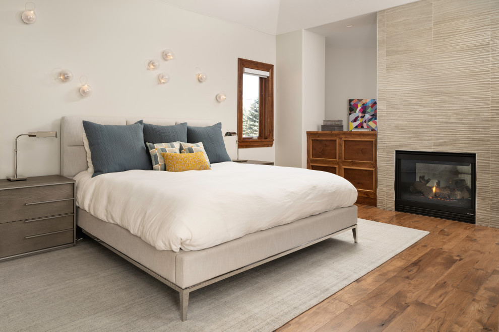 Großes Modernes Hauptschlafzimmer mit weißer Wandfarbe, braunem Holzboden, gefliester Kaminumrandung, braunem Boden, Tunnelkamin und gewölbter Decke in Denver