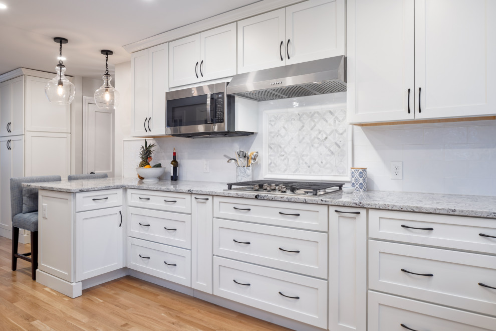 Mid-sized transitional u-shaped medium tone wood floor eat-in kitchen photo in Boston with a farmhouse sink, shaker cabinets, white cabinets, granite countertops, white backsplash, subway tile backsplash, stainless steel appliances, a peninsula and multicolored countertops
