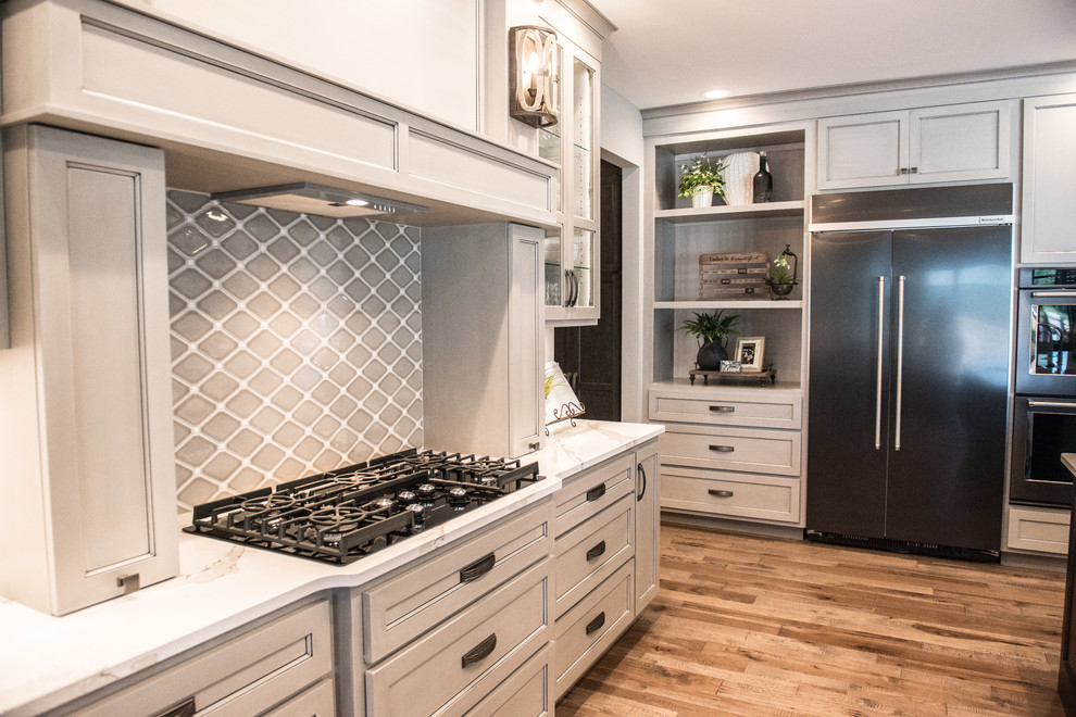 Example of a huge transitional l-shaped medium tone wood floor and brown floor open concept kitchen design with a single-bowl sink, glass-front cabinets, gray cabinets, quartz countertops, gray backsplash, mirror backsplash, stainless steel appliances, an island and white countertops