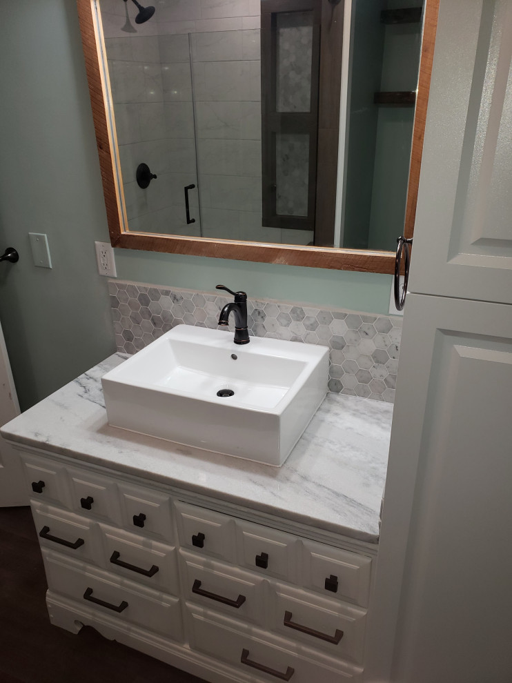 This is an example of a mid-sized country 3/4 bathroom in Other with recessed-panel cabinets, white cabinets, an alcove shower, a two-piece toilet, gray tile, marble, green walls, laminate floors, a vessel sink, quartzite benchtops, brown floor, a hinged shower door, grey benchtops, a shower seat, a single vanity and a freestanding vanity.