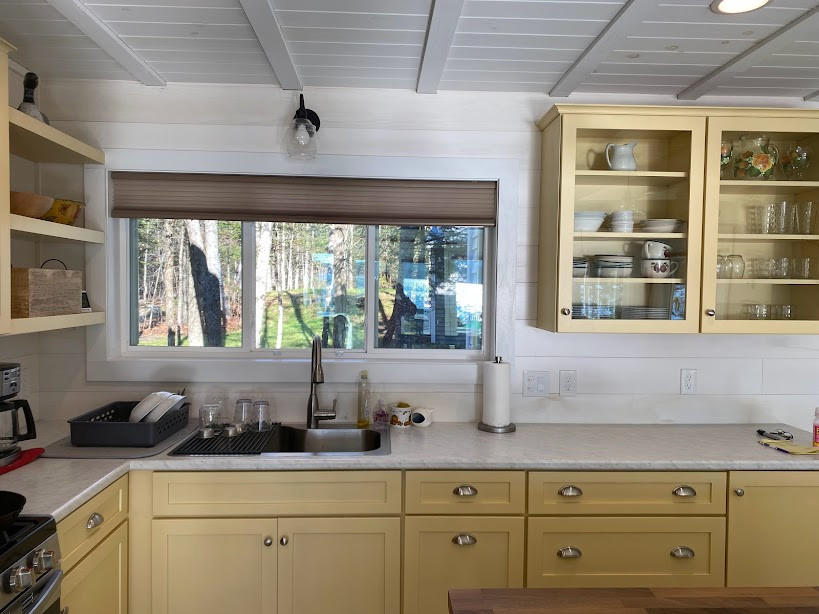 This is an example of a mid-sized scandinavian l-shaped open plan kitchen in Other with a single-bowl sink, recessed-panel cabinets, yellow cabinets, laminate benchtops, stainless steel appliances, concrete floors, with island, beige floor, grey benchtop and exposed beam.