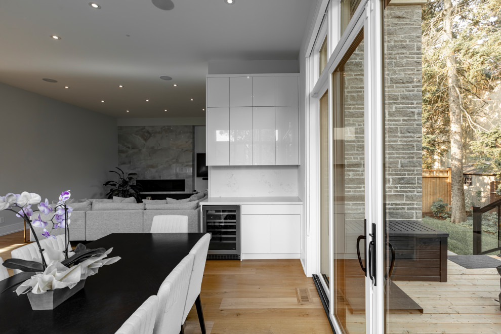 This is an example of a large contemporary l-shaped eat-in kitchen in Toronto with an undermount sink, flat-panel cabinets, white cabinets, quartz benchtops, white splashback, engineered quartz splashback, panelled appliances, light hardwood floors, with island, beige floor and white benchtop.