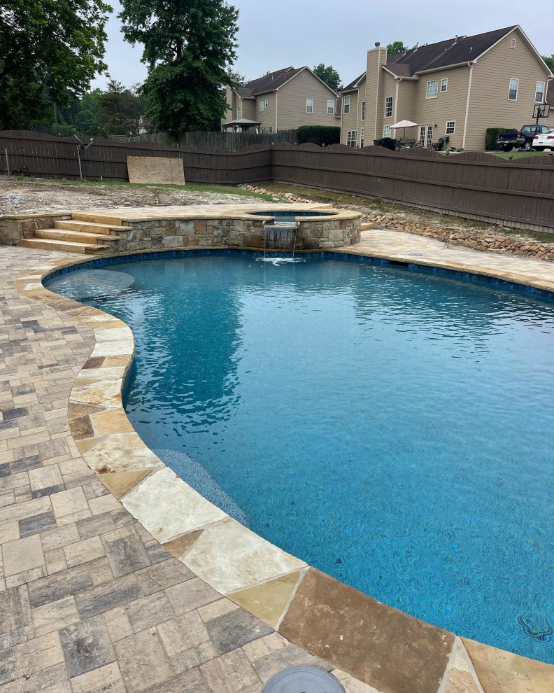 Photo of a large backyard kidney-shaped natural pool with a hot tub and brick pavers.