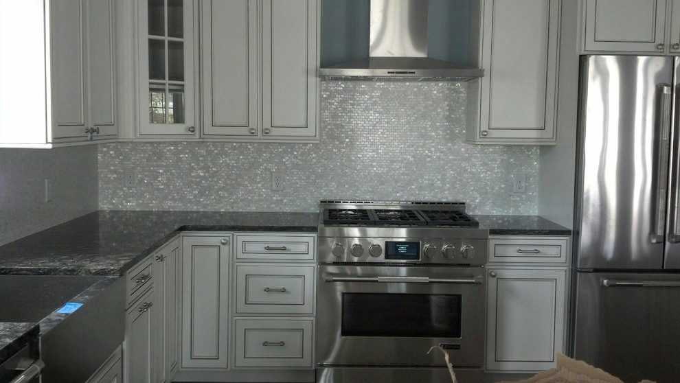 Mid-sized transitional kitchen photo in New York with a farmhouse sink, recessed-panel cabinets, white cabinets, granite countertops, metallic backsplash, metal backsplash, stainless steel appliances and an island