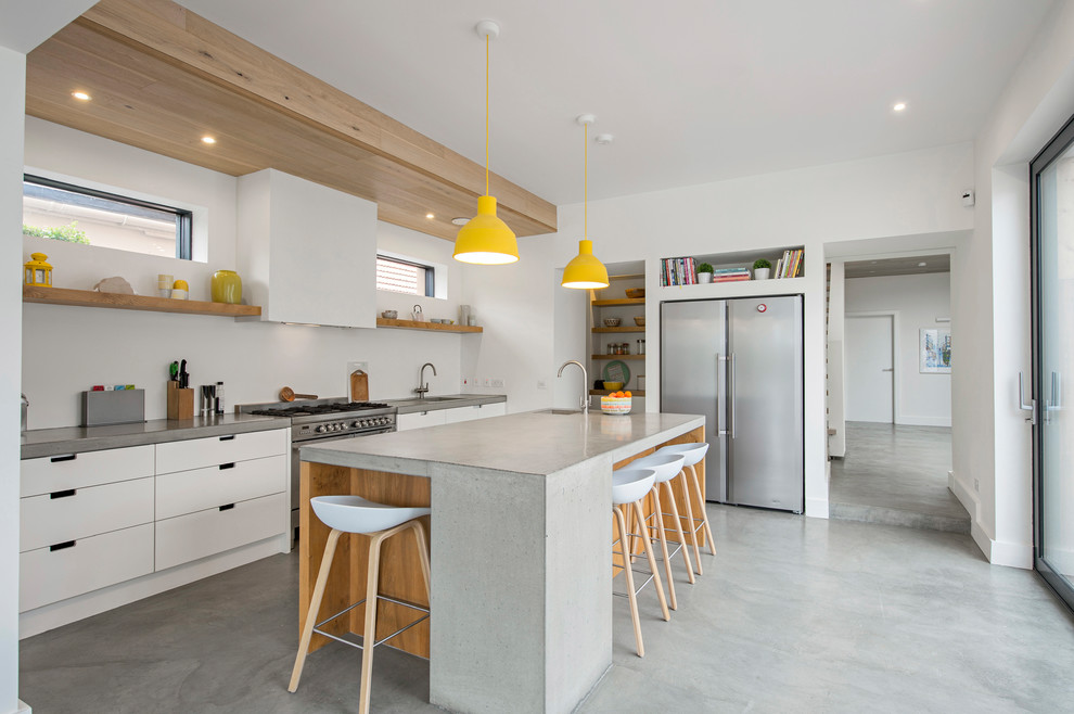 Inspiration for a mid-sized industrial single-wall kitchen in Dublin with flat-panel cabinets, white cabinets, concrete benchtops, white splashback, concrete floors, with island, grey floor and stainless steel appliances.