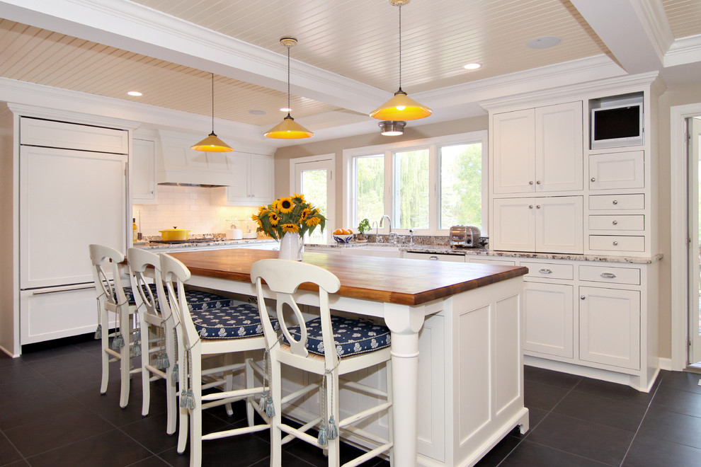 Photo of a traditional l-shaped eat-in kitchen in Minneapolis with recessed-panel cabinets, a farmhouse sink, white cabinets, granite benchtops, white splashback, subway tile splashback, panelled appliances, slate floors and with island.
