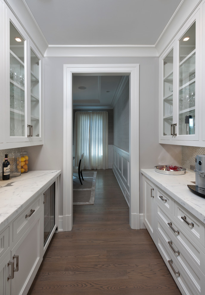 Photo of a small transitional galley kitchen pantry in New York with recessed-panel cabinets, white cabinets, an undermount sink, marble benchtops, metallic splashback, white appliances and medium hardwood floors.