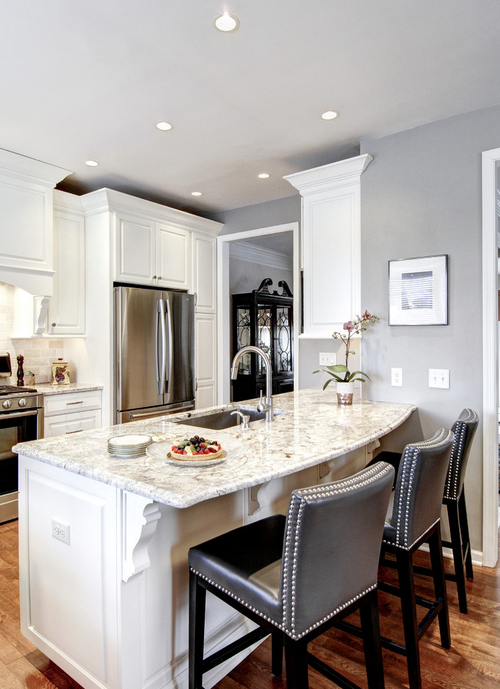 This is an example of a contemporary single-wall eat-in kitchen in Philadelphia with an undermount sink, raised-panel cabinets, white cabinets, marble benchtops, white splashback, stone tile splashback, stainless steel appliances, medium hardwood floors and with island.