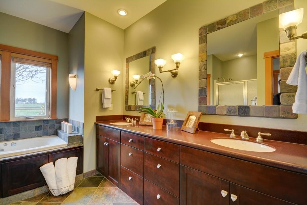 Photo of an arts and crafts master bathroom in Seattle with an undermount sink, flat-panel cabinets, dark wood cabinets, solid surface benchtops, a drop-in tub, an alcove shower, a two-piece toilet, terra-cotta tile and travertine floors.