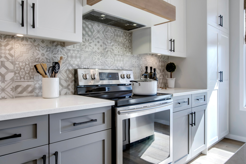 Photo of a mid-sized country l-shaped eat-in kitchen in Calgary with an undermount sink, shaker cabinets, quartz benchtops, cement tile splashback, stainless steel appliances, light hardwood floors, with island, beige floor and white benchtop.