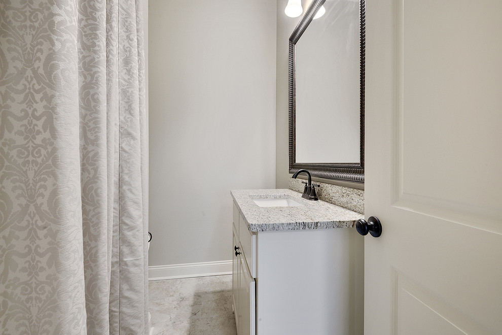 This is an example of a small traditional 3/4 bathroom in New Orleans with raised-panel cabinets, white cabinets, a drop-in tub, a shower/bathtub combo, a two-piece toilet, beige tile, ceramic tile, beige walls, ceramic floors, an undermount sink, granite benchtops, beige floor and a shower curtain.