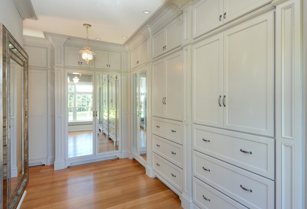 Inspiration for a large transitional gender-neutral walk-in wardrobe in Boston with shaker cabinets, white cabinets and light hardwood floors.