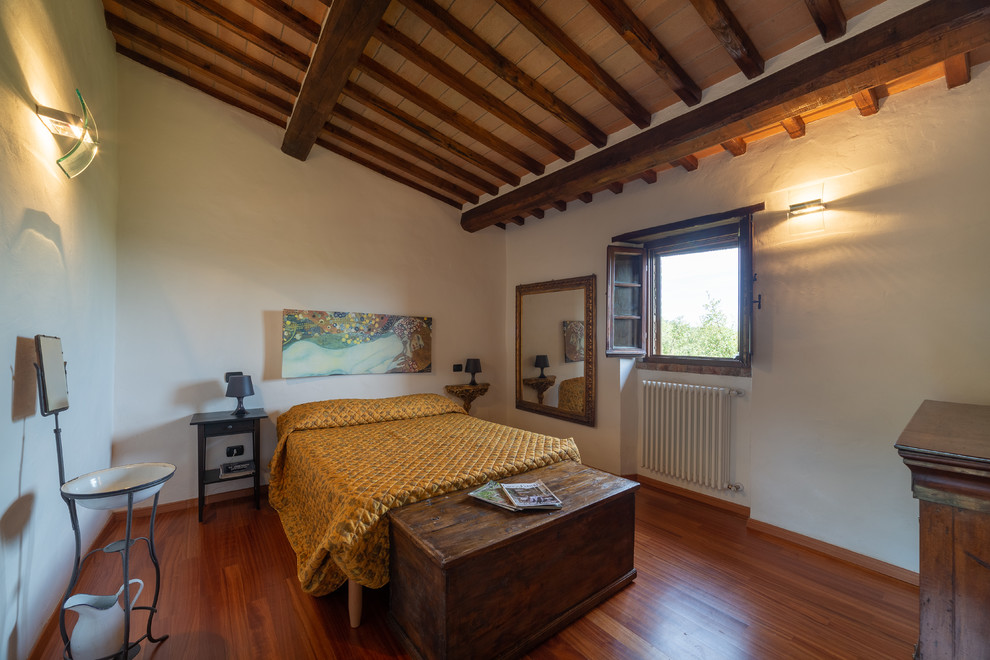 Photo of a country bedroom in Florence with white walls, medium hardwood floors and brown floor.
