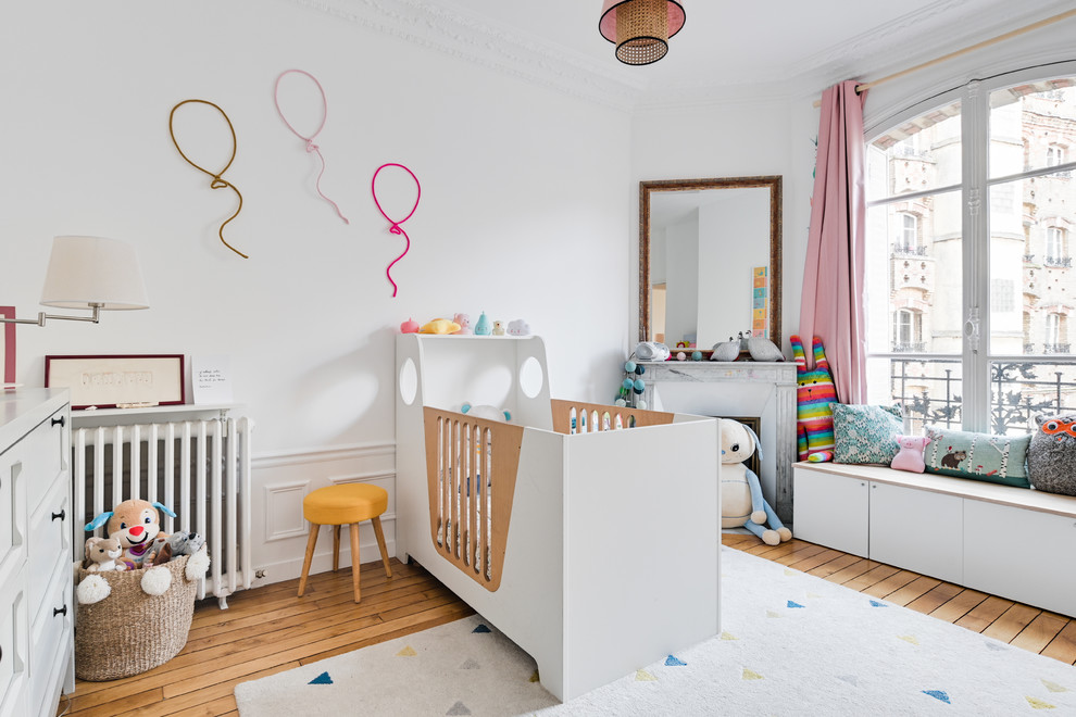 Exemple de chambre de bébé fille pour fille avec un mur blanc et parquet clair.