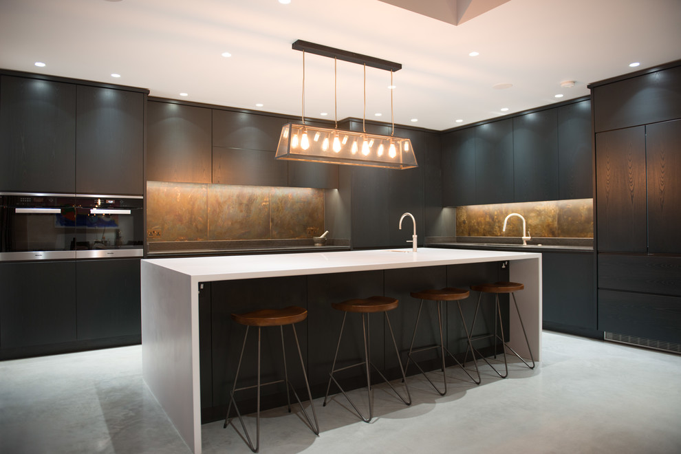 This is an example of an expansive modern l-shaped open plan kitchen in London with a drop-in sink, flat-panel cabinets, dark wood cabinets, quartzite benchtops, multi-coloured splashback, metal splashback, stainless steel appliances, concrete floors, with island, grey floor and white benchtop.