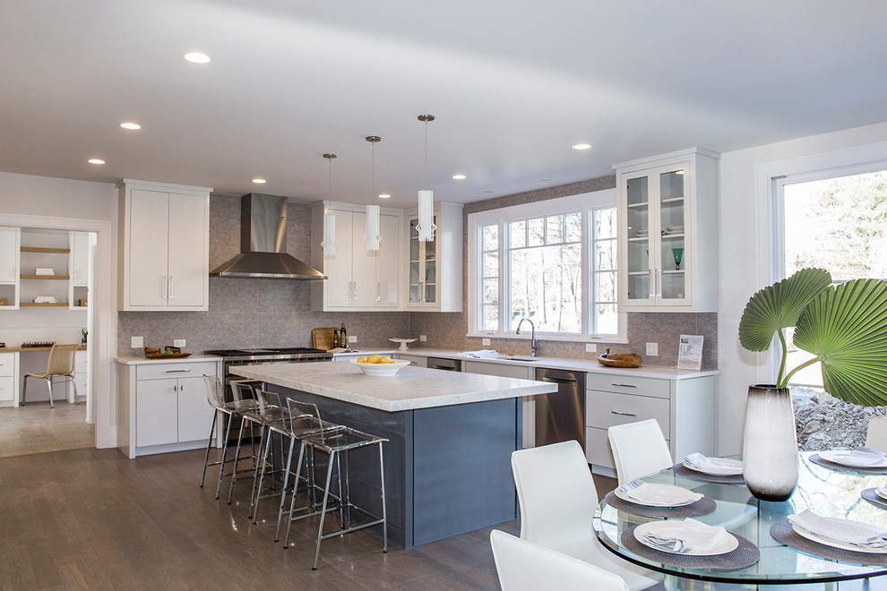 This is an example of a transitional u-shaped eat-in kitchen in New York with an undermount sink, flat-panel cabinets, white cabinets, grey splashback, stainless steel appliances, with island, brown floor and white benchtop.