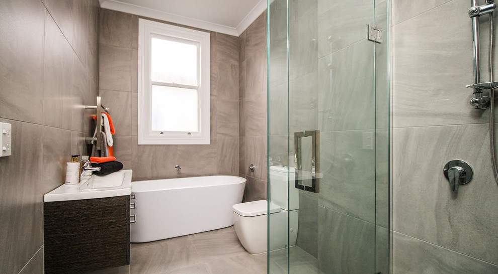 This is an example of a small traditional bathroom in Auckland with flat-panel cabinets, dark wood cabinets, a freestanding tub, a corner shower, a two-piece toilet, gray tile, stone tile, a drop-in sink, grey floor and a hinged shower door.