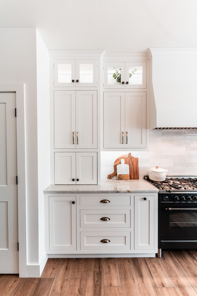 Example of a large transitional l-shaped light wood floor open concept kitchen design with an undermount sink, shaker cabinets, white cabinets, quartzite countertops, multicolored backsplash, porcelain backsplash, stainless steel appliances and an island