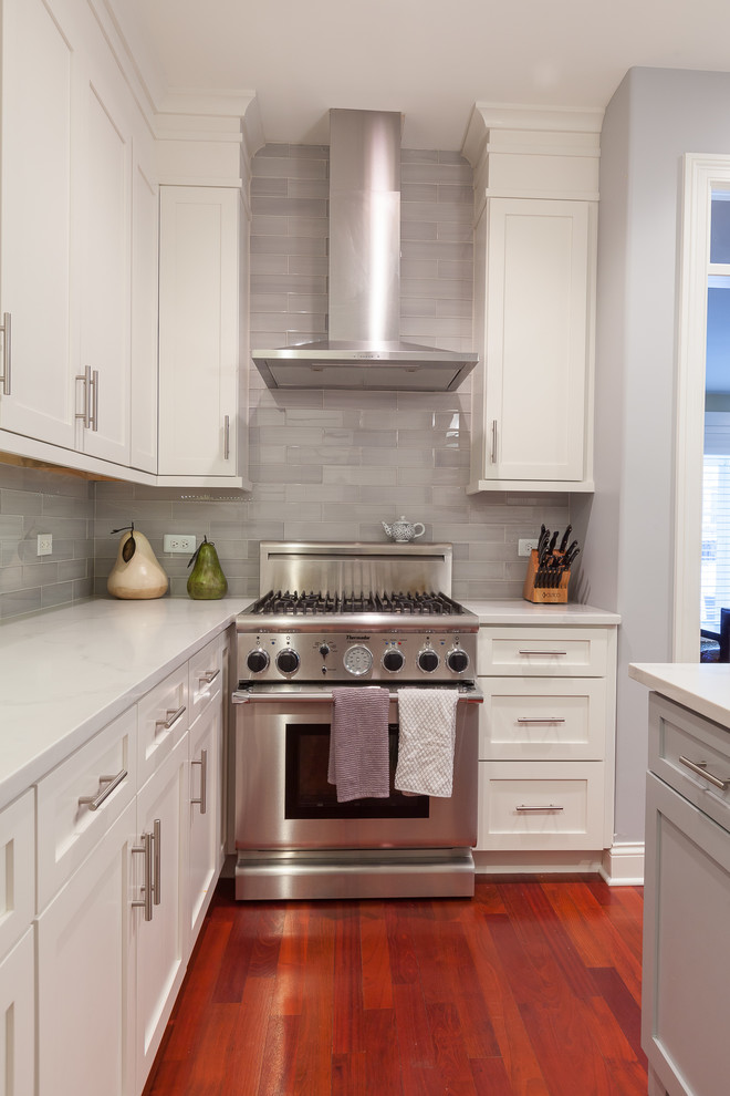 This is an example of a large transitional u-shaped eat-in kitchen in Chicago with an undermount sink, shaker cabinets, white cabinets, quartz benchtops, grey splashback, glass tile splashback, stainless steel appliances, medium hardwood floors, with island and red floor.