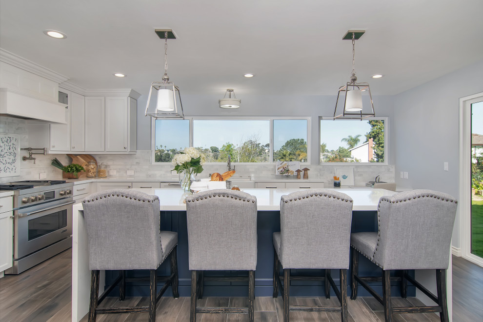 This is an example of a large traditional l-shaped kitchen in San Diego with a farmhouse sink, shaker cabinets, white cabinets, grey splashback, stainless steel appliances, with island, grey floor and white benchtop.