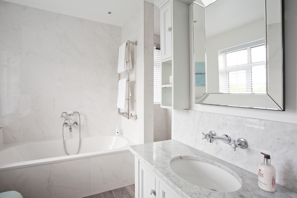 Photo of a mid-sized traditional master bathroom in Sussex with shaker cabinets, white cabinets, a drop-in tub, a shower/bathtub combo, a wall-mount toilet, gray tile, marble, grey walls, laminate floors, an integrated sink, grey floor and an open shower.