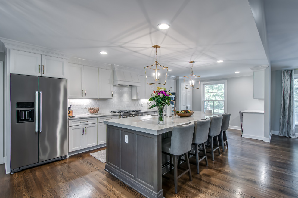 Photo of a transitional galley kitchen in Nashville with an undermount sink, recessed-panel cabinets, white cabinets, white splashback, mosaic tile splashback, stainless steel appliances, dark hardwood floors, with island, brown floor and white benchtop.