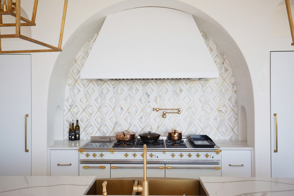 Bild på ett stort maritimt vit linjärt vitt kök och matrum, med en rustik diskho, släta luckor, vita skåp, bänkskiva i kvarts, vitt stänkskydd, integrerade vitvaror, en köksö och beiget golv