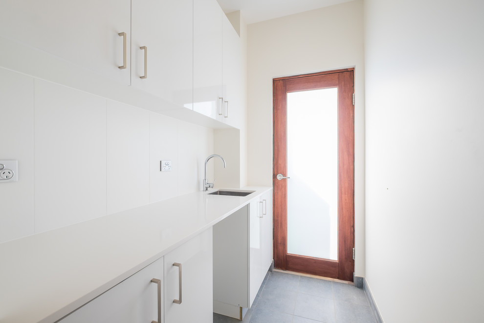 This is an example of a modern galley utility room in Sydney with an undermount sink, raised-panel cabinets, white cabinets, limestone benchtops, white walls and ceramic floors.