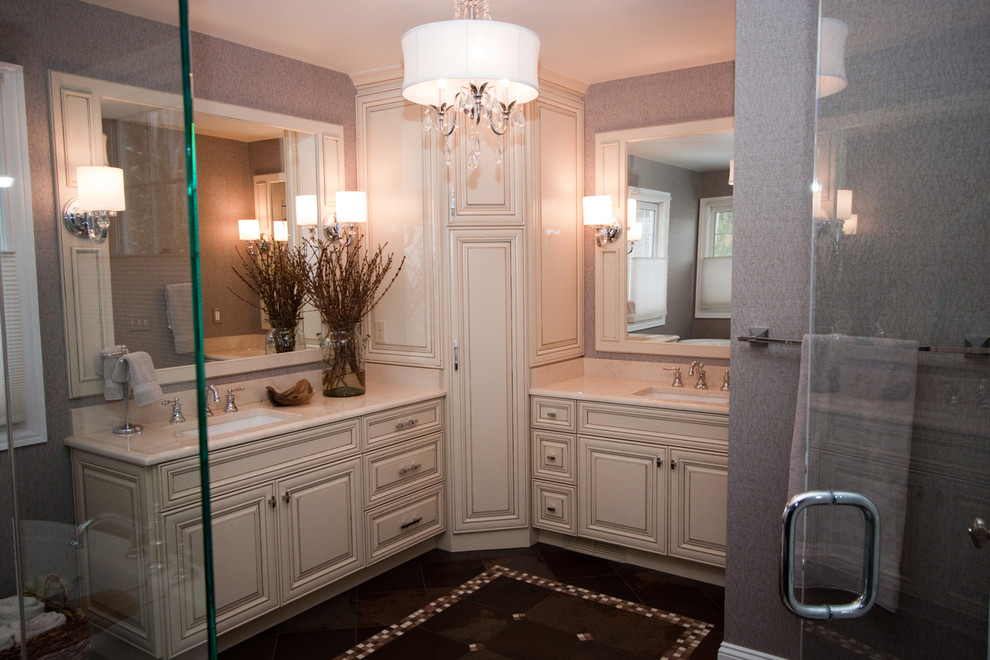 Inspiration for a mid-sized traditional master bathroom in Cleveland with raised-panel cabinets, beige cabinets, beige tile, stone slab, solid surface benchtops, a freestanding tub, a corner shower, a two-piece toilet, grey walls, ceramic floors, an undermount sink, brown floor and a hinged shower door.