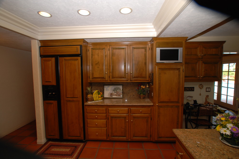 This is an example of a mid-sized traditional u-shaped open plan kitchen in Orange County with a double-bowl sink, raised-panel cabinets, medium wood cabinets, granite benchtops, beige splashback, stone slab splashback, panelled appliances, terra-cotta floors and a peninsula.