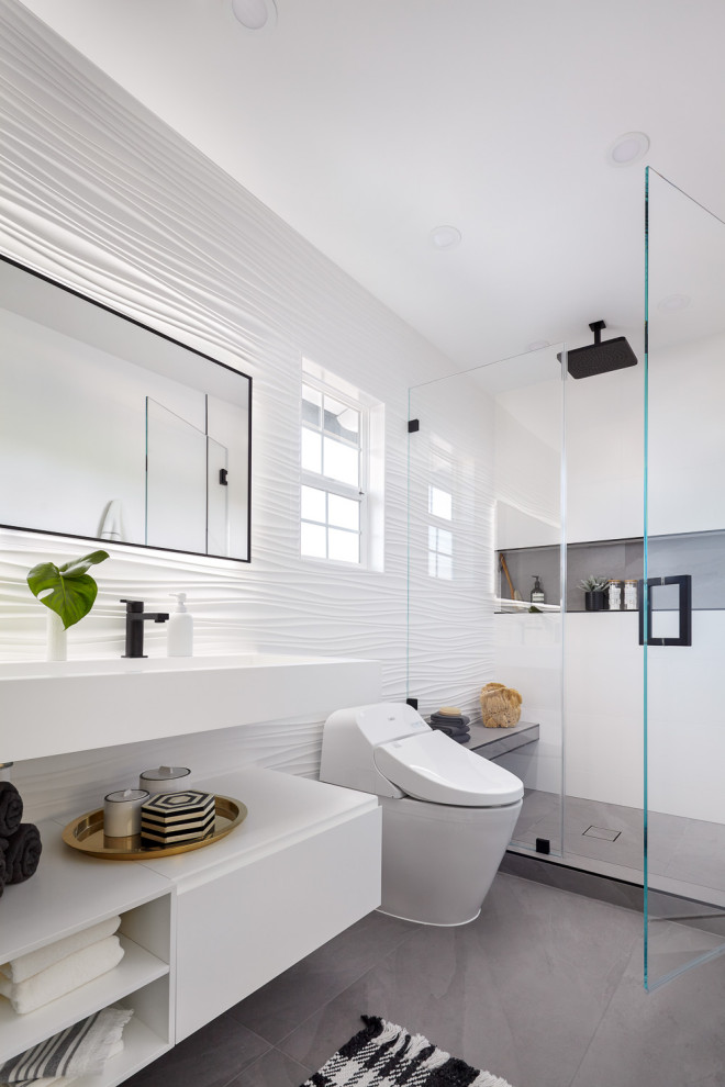 Стильный дизайн: большая главная ванная комната в стиле модернизм с плоскими фасадами, белыми фасадами, душем в нише, инсталляцией, белой плиткой, керамогранитной плиткой, серыми стенами, полом из керамогранита, монолитной раковиной, столешницей из искусственного кварца, серым полом, душем с распашными дверями, белой столешницей, сиденьем для душа, тумбой под две раковины и подвесной тумбой - последний тренд