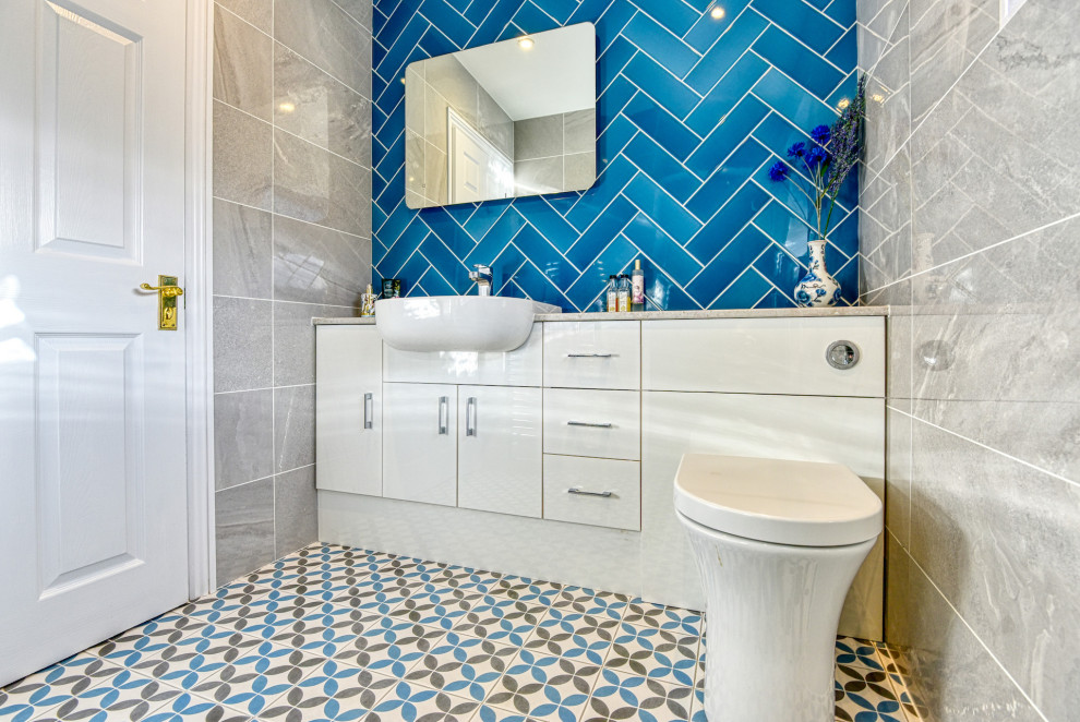 Exempel på ett mellanstort modernt beige beige badrum med dusch, med släta luckor, beige skåp, en dusch i en alkov, en vägghängd toalettstol, blå kakel, tunnelbanekakel, beige väggar, klinkergolv i keramik, ett konsol handfat, laminatbänkskiva, flerfärgat golv och dusch med gångjärnsdörr
