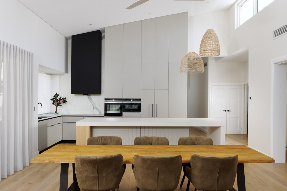Eat-in kitchen - large scandinavian l-shaped light wood floor, beige floor and vaulted ceiling eat-in kitchen idea in Perth with a double-bowl sink, flat-panel cabinets, gray cabinets, quartz countertops, white backsplash, porcelain backsplash, black appliances, an island and white countertops