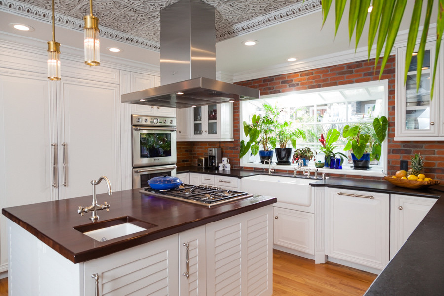 This is an example of a large beach style u-shaped kitchen in Los Angeles with a farmhouse sink, recessed-panel cabinets, white cabinets, granite benchtops, stainless steel appliances, light hardwood floors and with island.